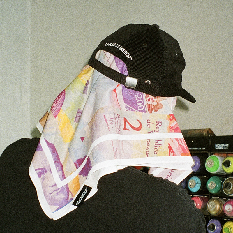 Bandana con el estampado de billetes de bolívar colocada sobre una gorra negra de Caracas Merch